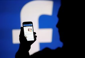 FILE PHOTO: A man is silhouetted against a video screen with an Facebook logo as he poses with an Samsung S4 smartphone in this photo illustration August 14, 2013. REUTERS/Dado Ruvic/File Photo - RC172F69CDF0